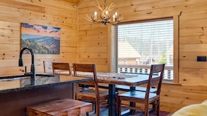 L’intérieur d’un chalet en bois comprend une table à manger, des chaises, un banc, un évier et un lustre.