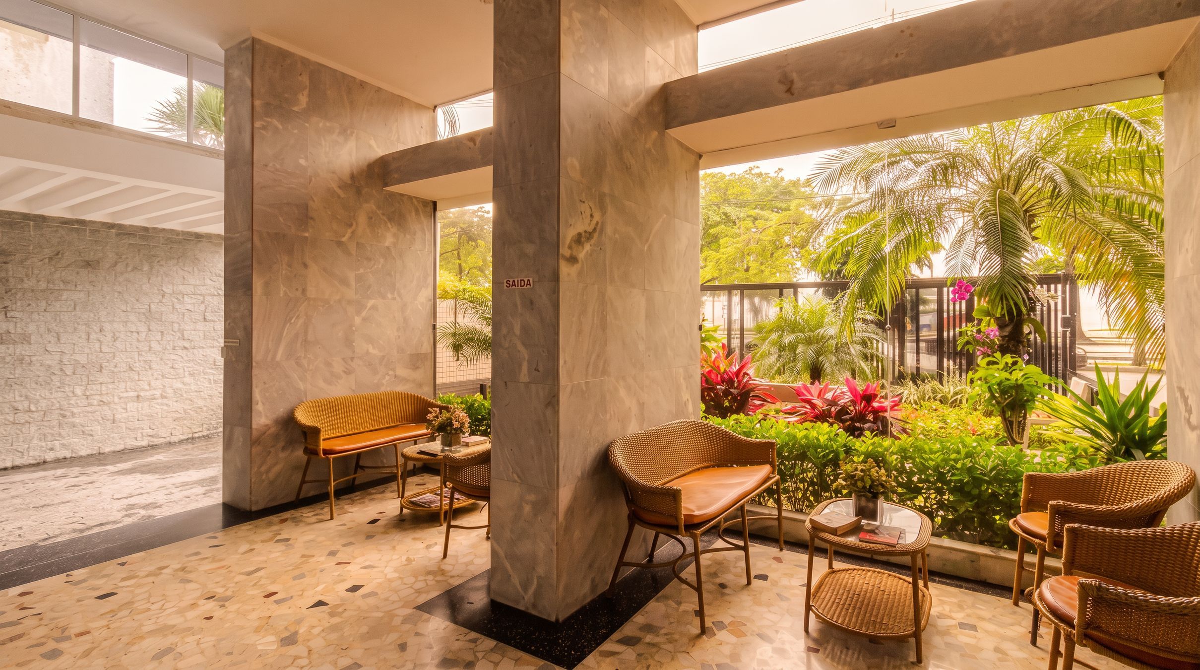 A spacious indoor area with a concrete floor, a brick wall, and a glass door leading to an outdoor garden.