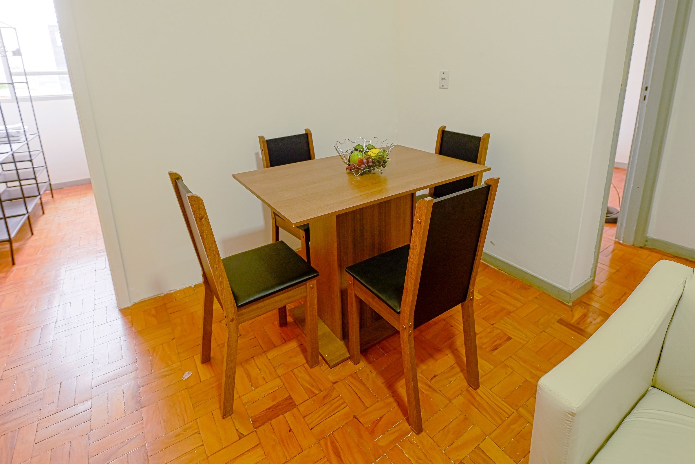 Un coin repas avec une table en bois et quatre chaises, un petit vase avec des fleurs et un mur blanc.