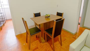 Un coin repas avec une table en bois et quatre chaises, un petit vase avec des fleurs et un mur blanc.