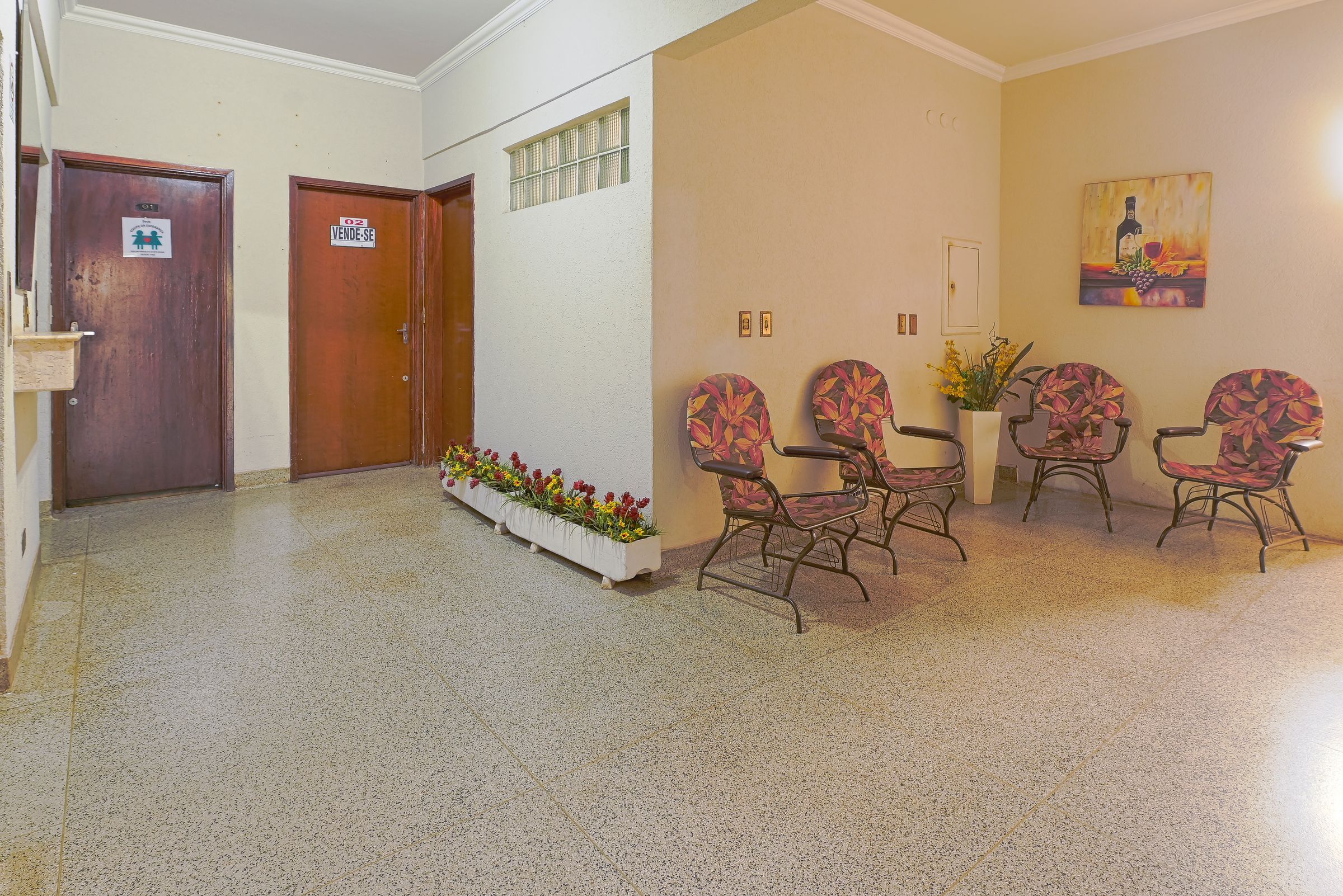 A hallway with a reception desk, a waiting area with chairs, a door marked 'VENDSE', and a small planter with flowers.