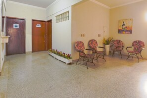 Um corredor com um balcão de recepção, uma área de espera com cadeiras, uma porta com a inscrição 'VENDSE' e um pequeno vaso com flores.