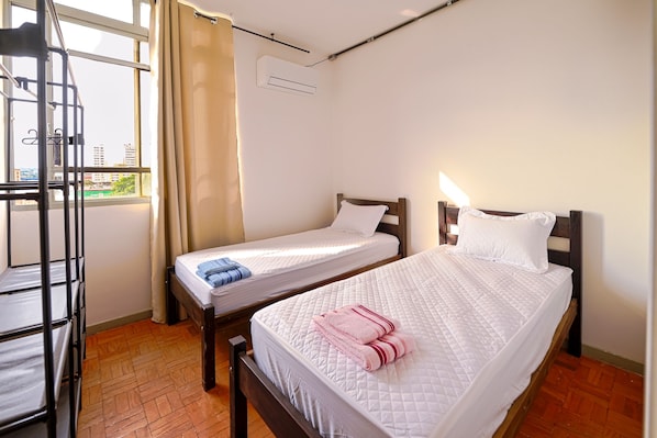 Quarto com duas camas, janela com cortinas, um suporte de metal e um aparelho de ar condicionado.