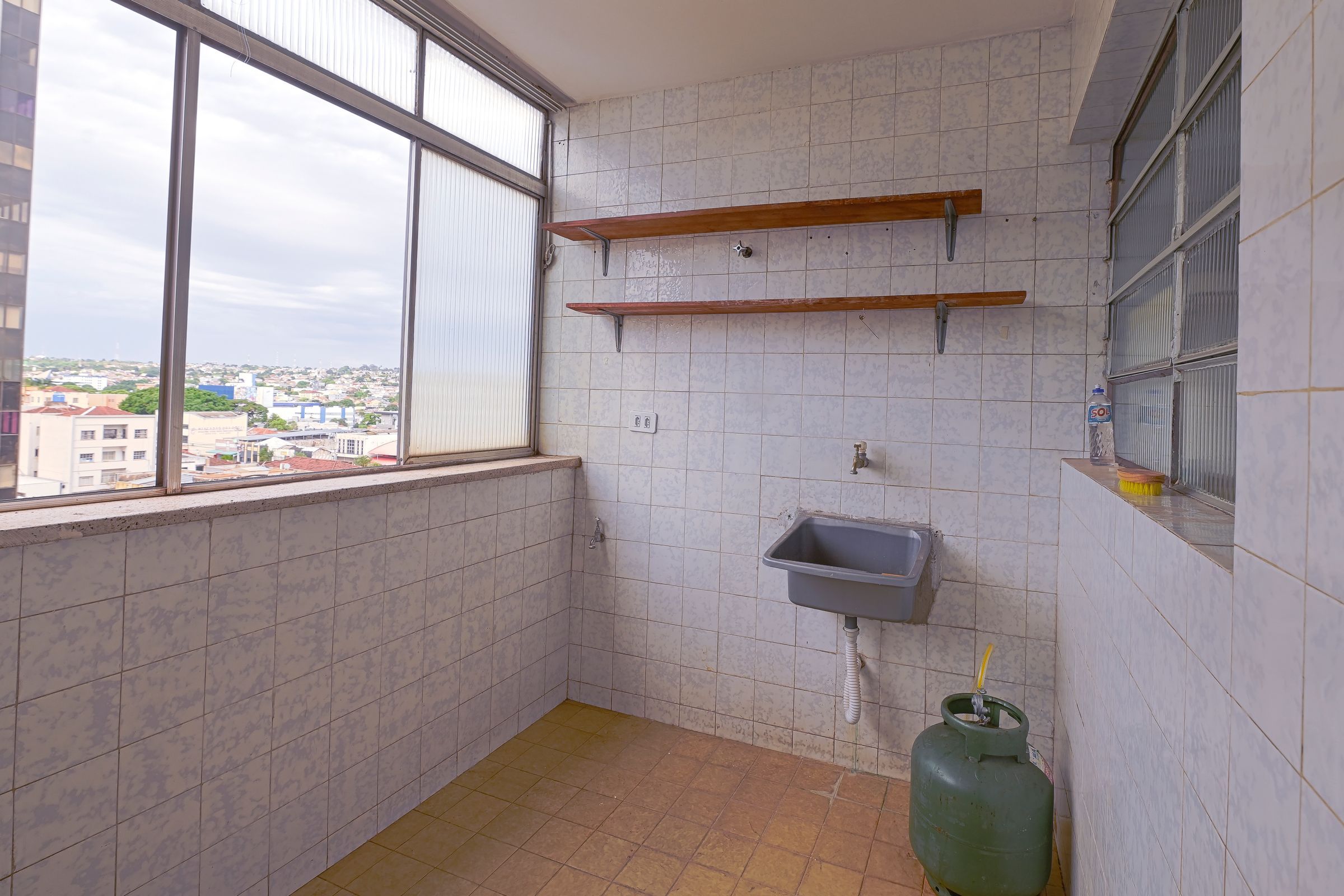 Casa de banho pequena com azulejos, uma janela, uma pia e um cilindro de gás.