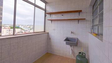 Casa de banho pequena com azulejos, uma janela, uma pia e um cilindro de gás.