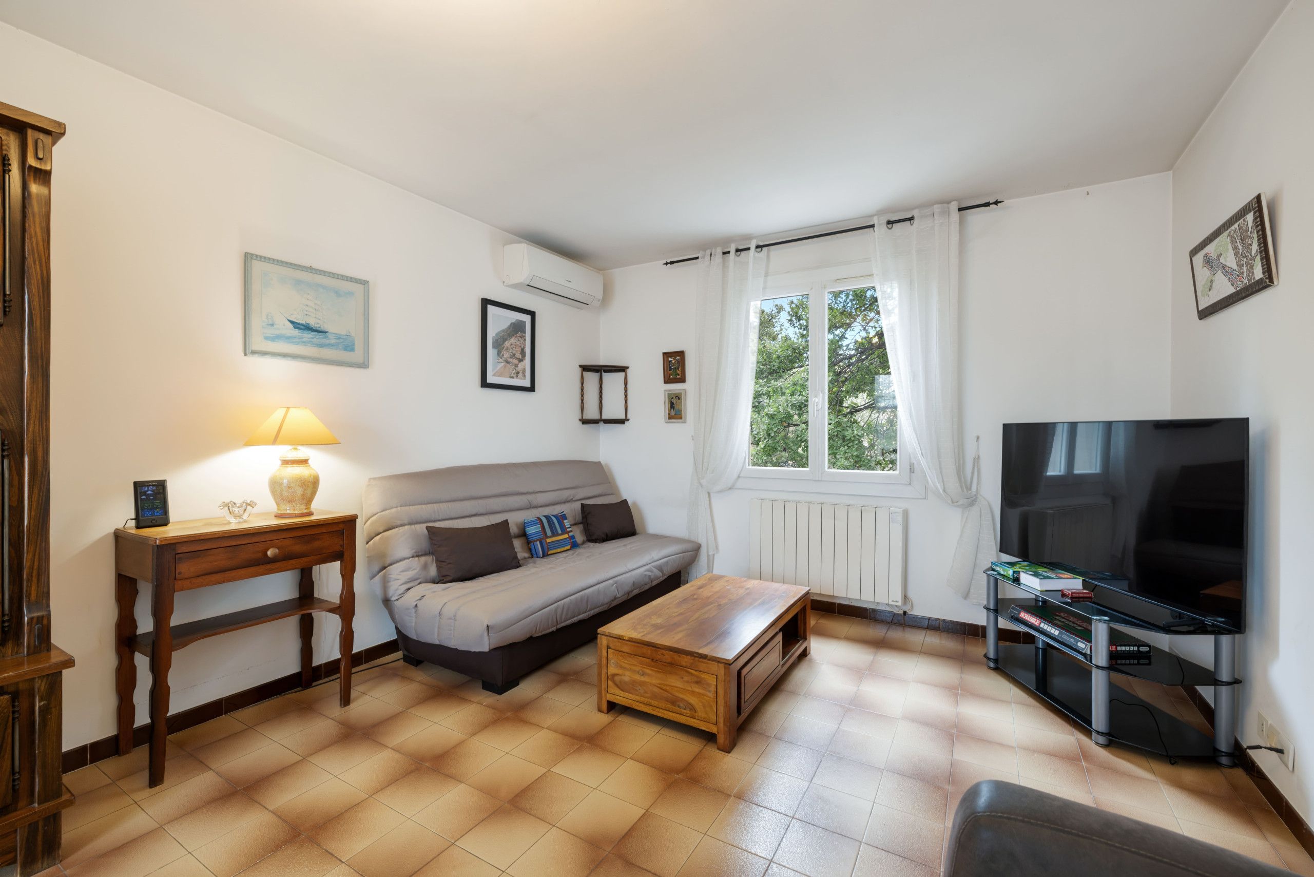 Een woonkamer met een bank, een salontafel, een televisie en een raam met gordijnen.