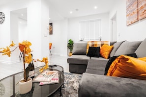 A modern living room with a grey sofa, orange cushions, a glass coffee table with magazines, and a potted plant. - Brighton St Merseyside 2-Bed/Sleeps 6 Wifi/Parking (Merseyside)