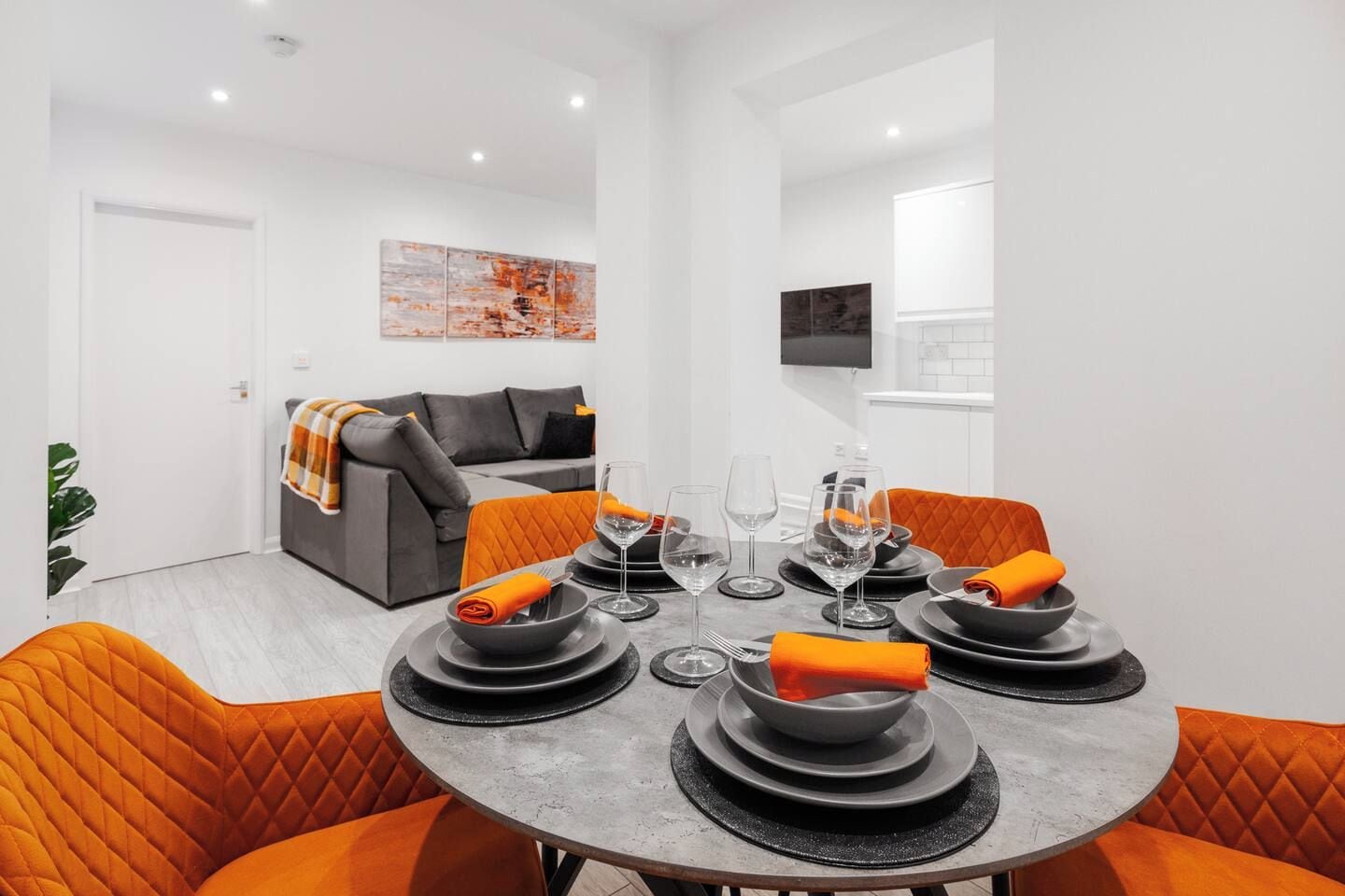 Comedor con una mesa redonda dispuesta para cuatro, platos grises y cojines anaranjados.