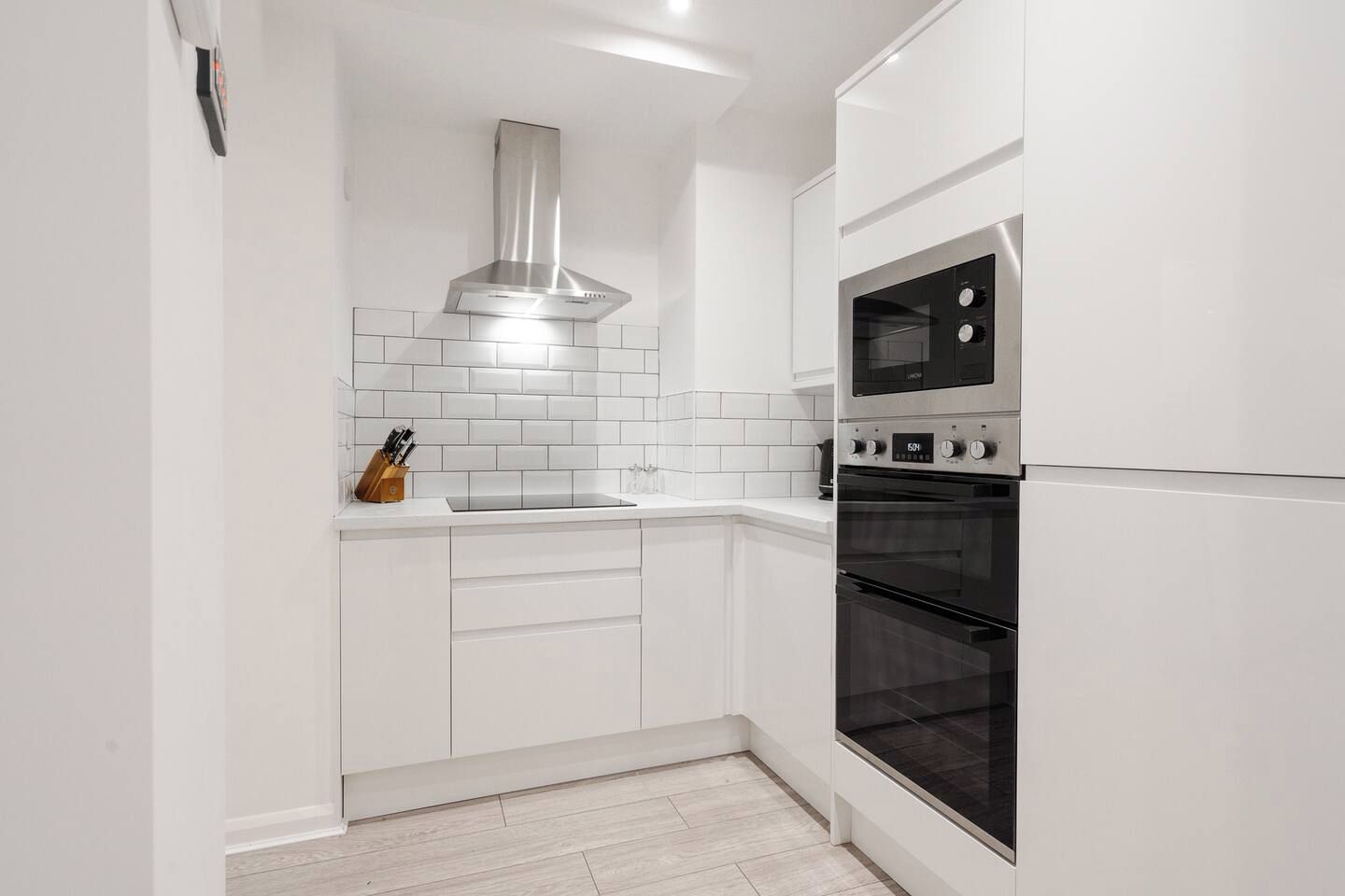 A modern kitchen with white cabinetry, a stainless steel range hood, a double oven, and a built-in microwave.