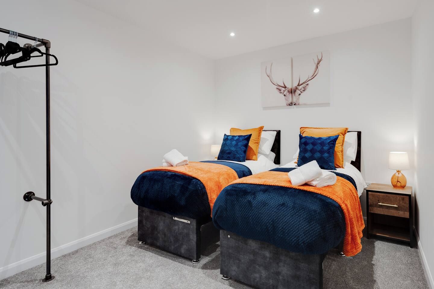 A hotel room with two beds, a standing lamp, a wall-mounted artwork, and a luggage trolley.