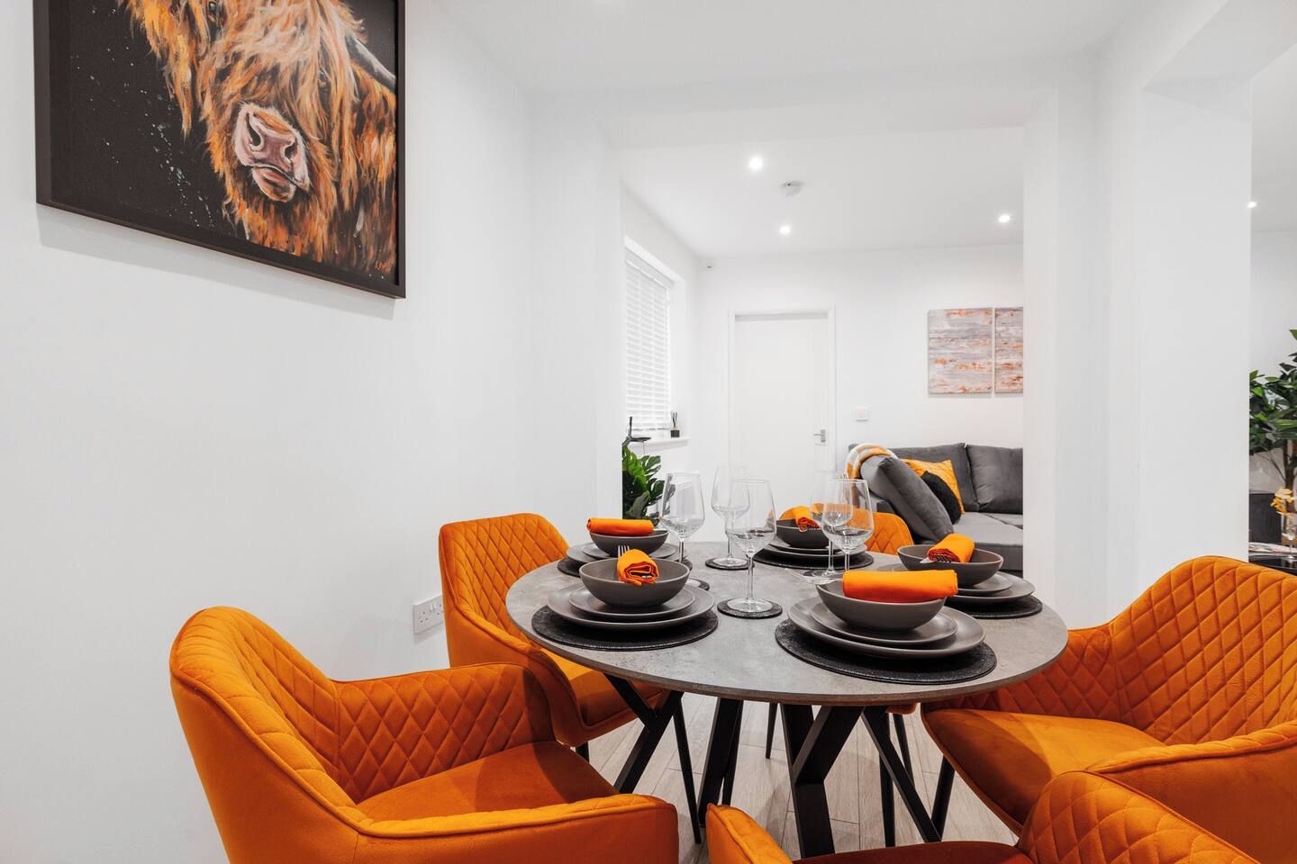 Un comedor con una mesa redonda, sillas naranjas y un cuadro en la pared.