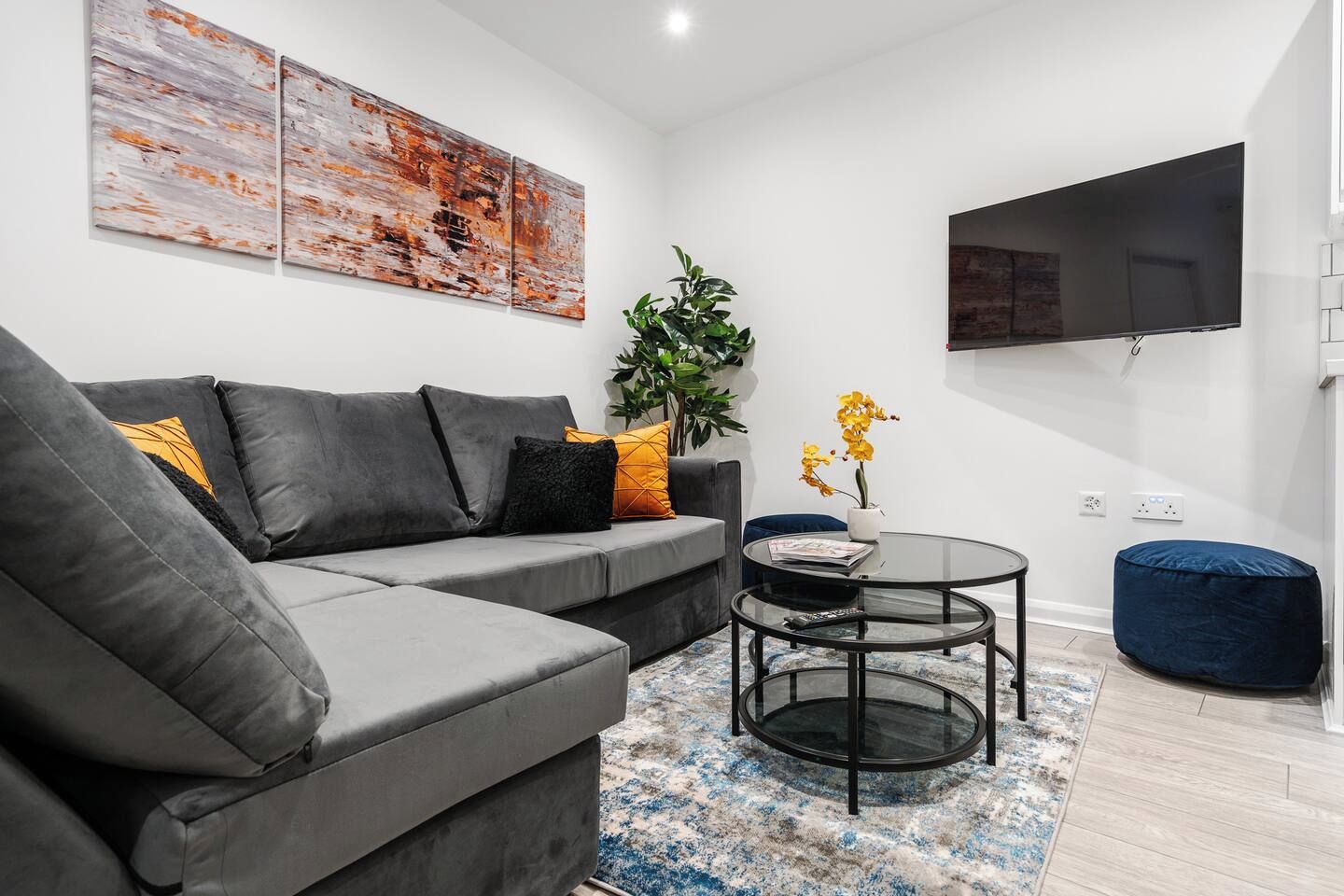 A modern living room with a grey sectional sofa, a round glass coffee table, and a blue bean bag.
