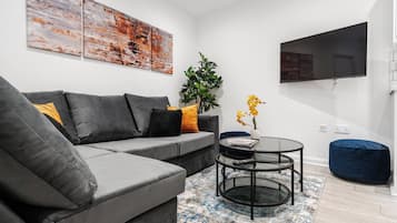 A modern living room with a grey sectional sofa, a round glass coffee table, and a blue bean bag.
