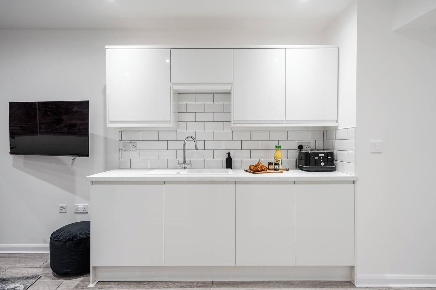 Une cuisine moderne avec des meubles blancs, un évier encastré et un téléviseur à écran plat fixé au mur.