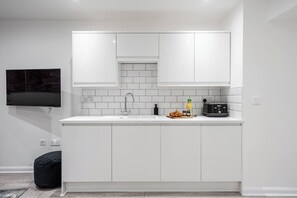 Een moderne keuken met witte kastjes, een ingebouwd spoelgedeelte en een flatscreen televisie aan de muur.