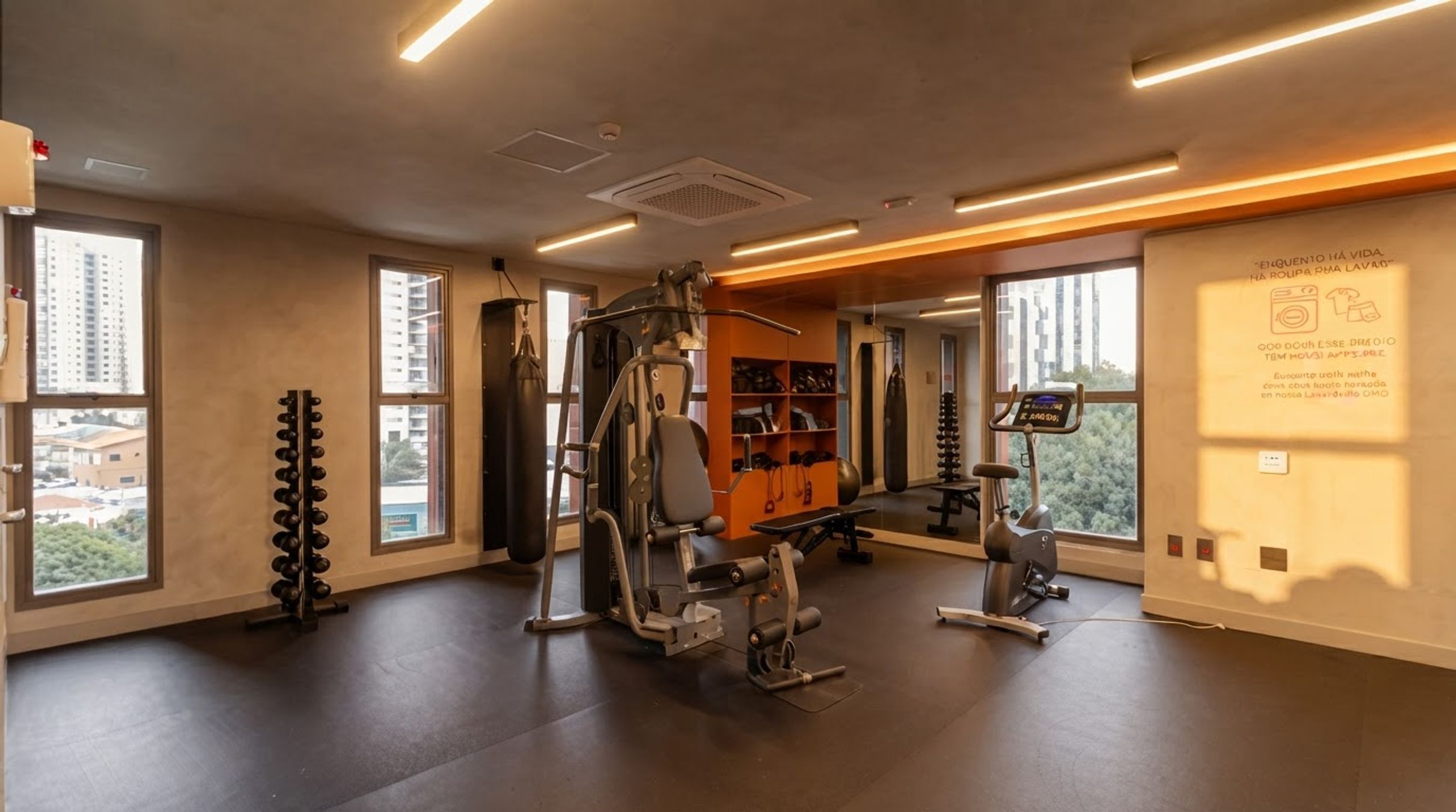 A gym with various exercise equipment, large windows, and a motivational quote on the wall.