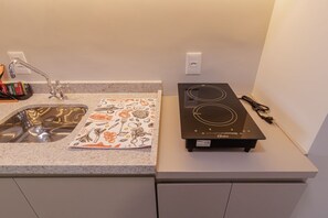 A kitchen with a stainless steel sink, a black induction cooktop, and a patterned cloth on the countertop. - Studio with Balcony and Pool | 140m from Sacomã Station (São Paulo)