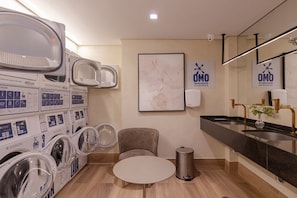A hotel room with a washing machine area, a sink with a mirror, a trash bin, and a framed map on the wall. - Studio with Balcony and Pool | 140m from Sacomã Station (São Paulo)