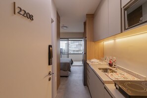 A modern kitchen with a built-in stove, a sink, and a window overlooking a balcony. - Studio with Balcony and Pool | 140m from Sacomã Station (São Paulo)