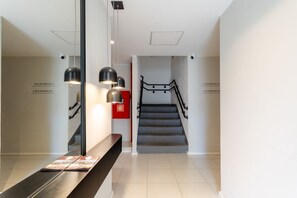 Un interior moderno con una escalera, un banco con folletos y luminarias colgantes.