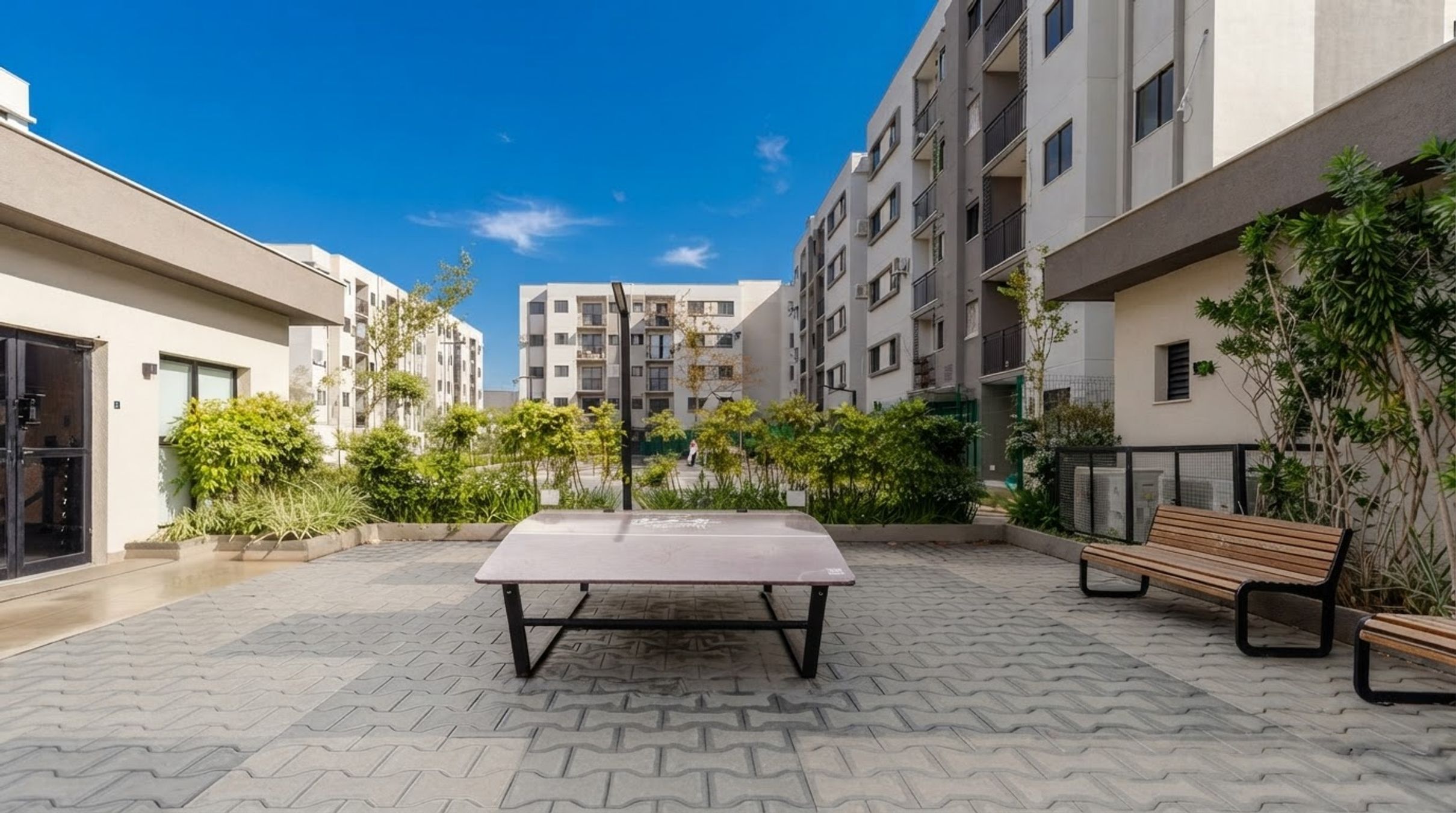 Une cour avec une table de ping-pong, des bancs et un bâtiment doté de plusieurs balcons.