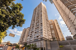 Un edificio alto con varios pisos, rodeado de otros edificios y árboles.