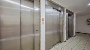 Ein Flur mit drei Aufzügen, jeweils mit metallischer Oberfläche und einem Rauchverbot-Schild.