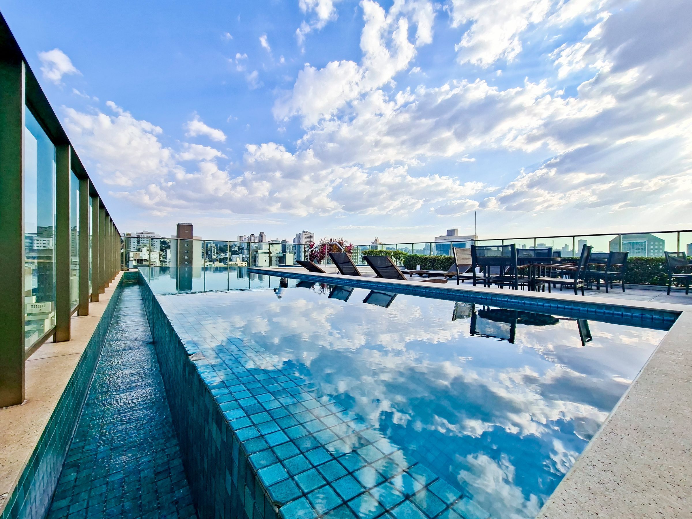 A rooftop infinity pool with lounge chairs and a cityscape view.