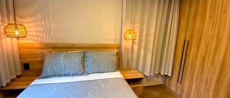 Un dormitorio con cama, cabecero de madera, dos lámparas de noche y un armario de madera.