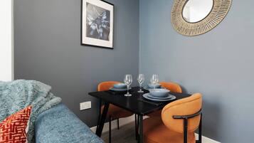 Ein Essbereich mit einem schwarzen Tisch, gedeckt für vier Personen, zwei orangefarbenen Stühlen und einem gerahmten Bild an der Wand.