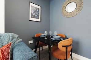 Ein Essbereich mit einem schwarzen Tisch, gedeckt für vier Personen, zwei orangefarbenen Stühlen und einem gerahmten Bild an der Wand.