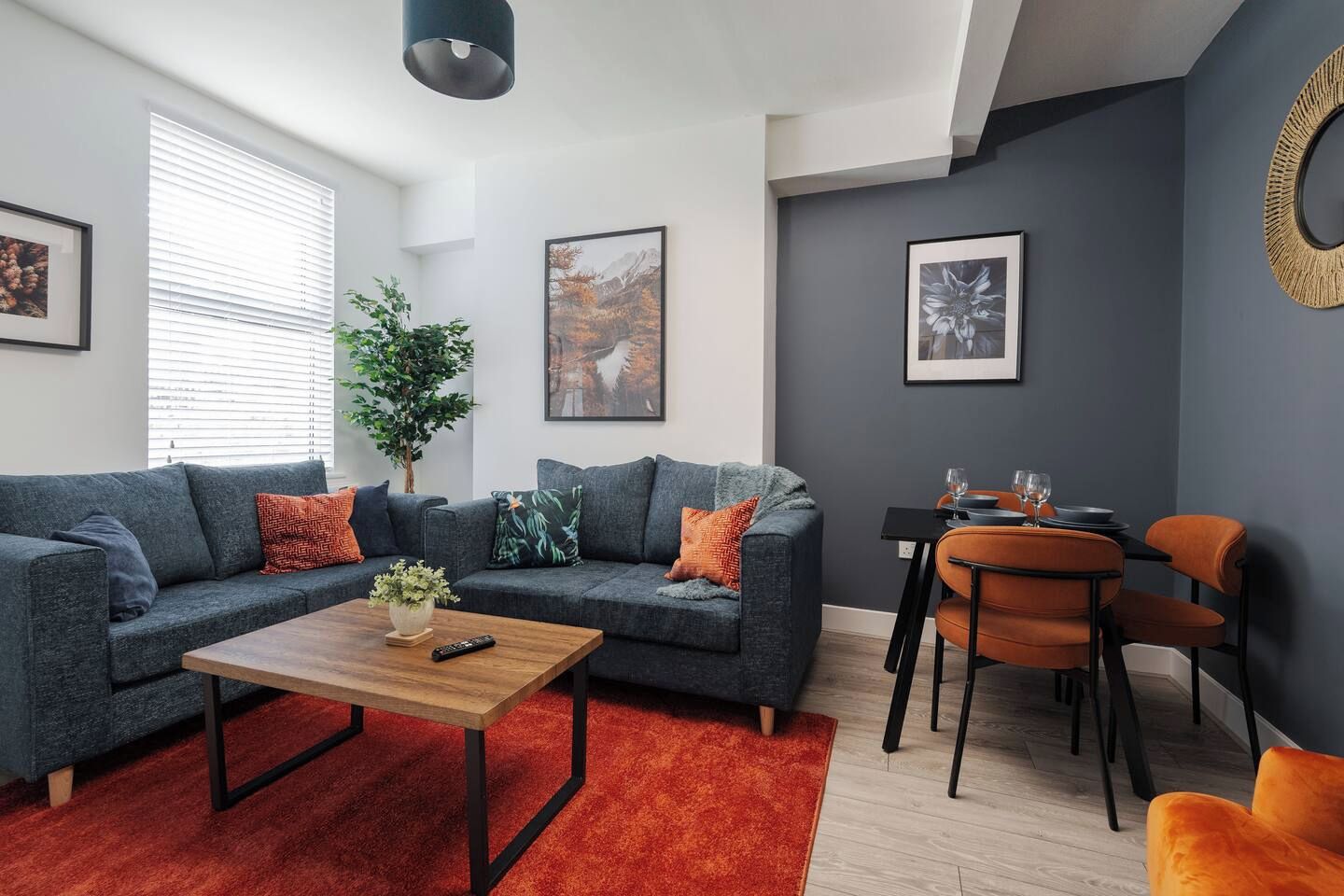 Ein modernes Wohnzimmer mit einem grauen Sofa, einem Holztisch und einem Essbereich mit orangefarbenen Stühlen.