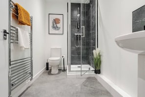 Ein modernes Badezimmer mit Duschkabine aus Glas, Toilette, Handtuchhalter und Waschbecken.
