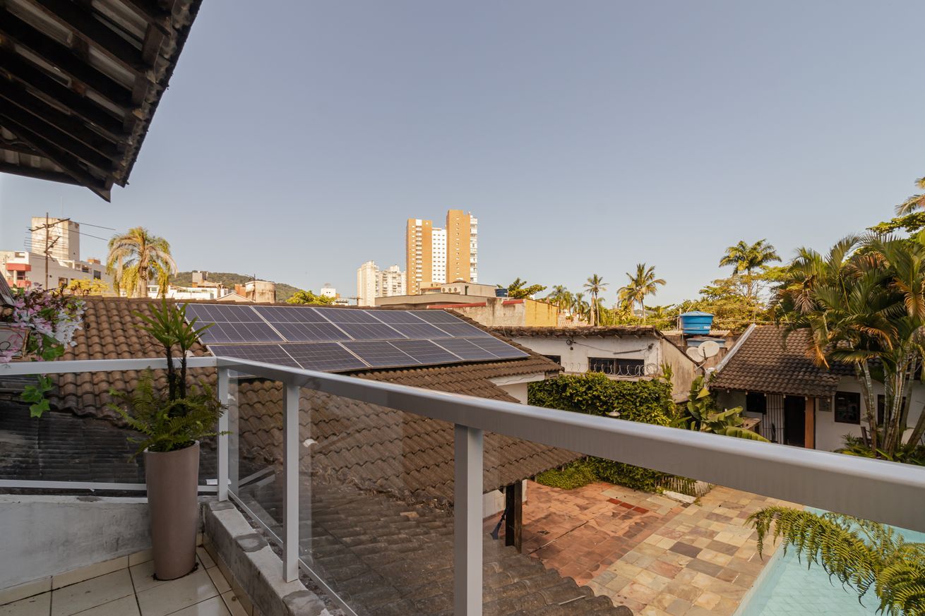 A residential area with solar panels on a rooftop, a balcony with a railing, and a view of surrounding buildings and palm trees.