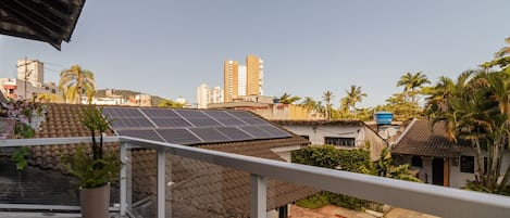 A residential area with solar panels on a rooftop, a balcony with a railing, and a view of surrounding buildings and palm trees.