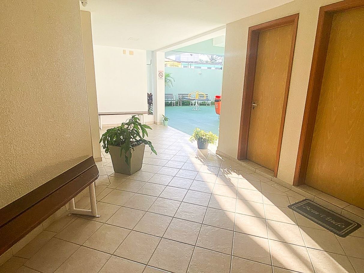 A corridor with a bench, potted plants, and a door leading to an outdoor area with a pool.