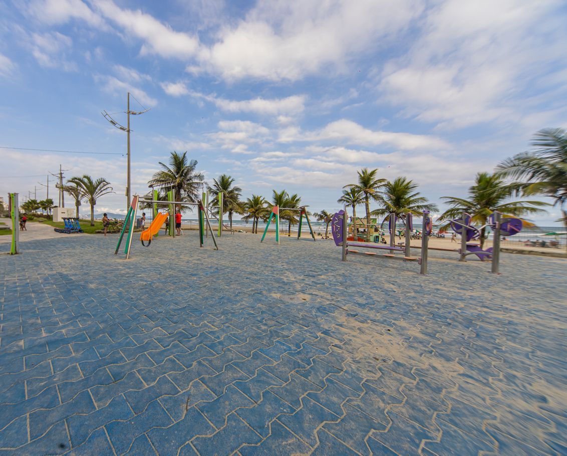 A beach playground with swings and slides, palm trees, and a clear sky.
