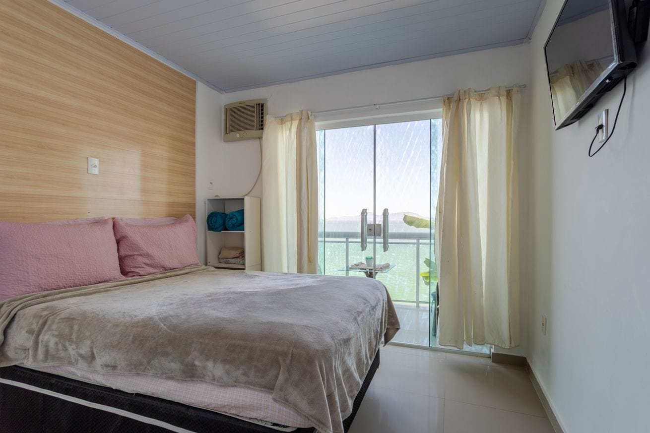 A hotel room with a bed, a TV, a window with curtains, and a balcony with a view.