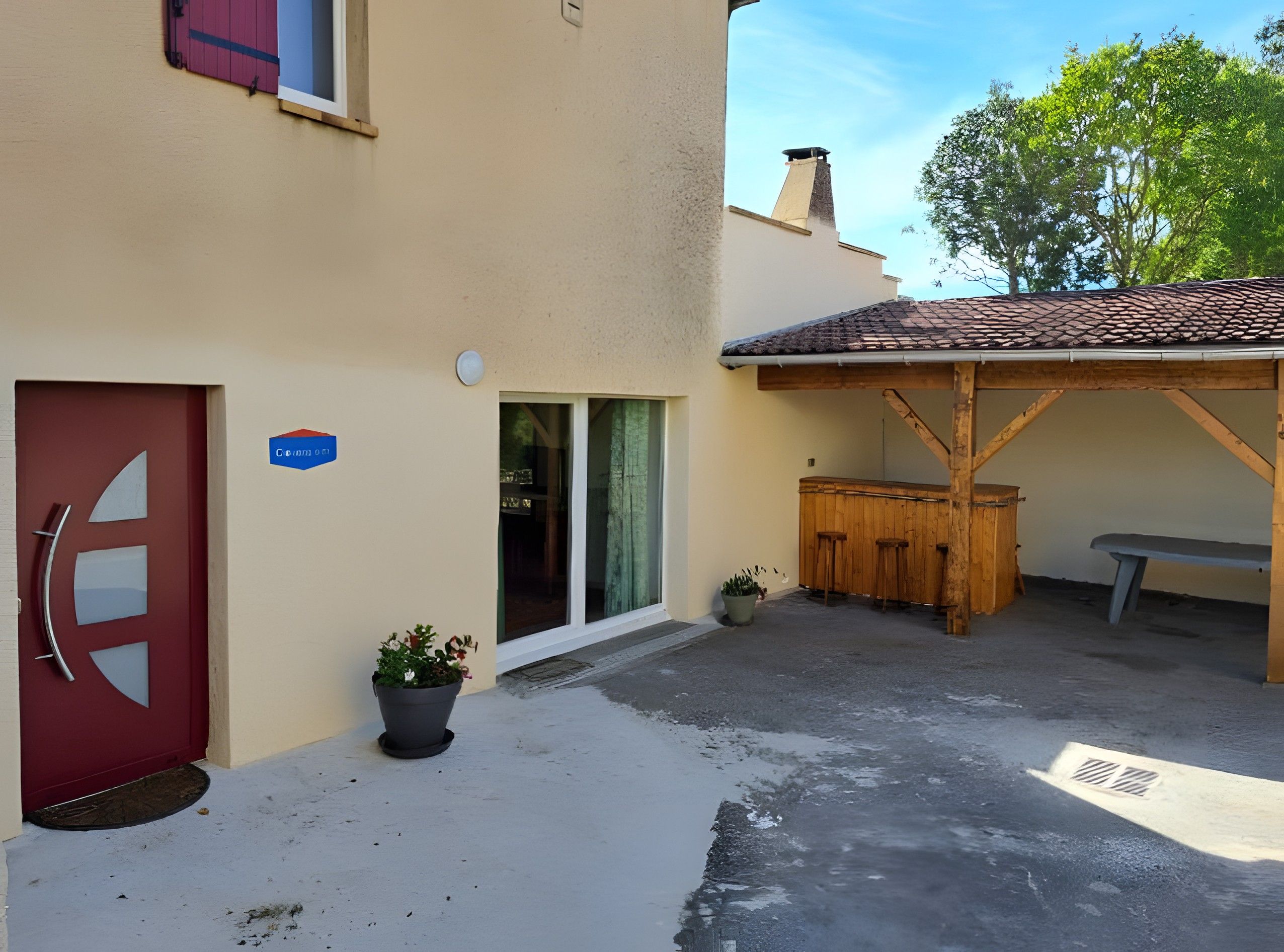 A building with a red door, a blue sign, a wooden bench, and a covered patio area.