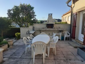An outdoor patio with a round table and chairs, a barbecue grill, and a wall-mounted sink.