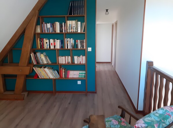 A room with a wooden staircase, a bookshelf filled with books, a wooden floor, and a bed with a floral pillow.