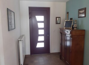 A hallway with a dark door, a radiator, a cabinet with a vase, and a framed picture on the wall.