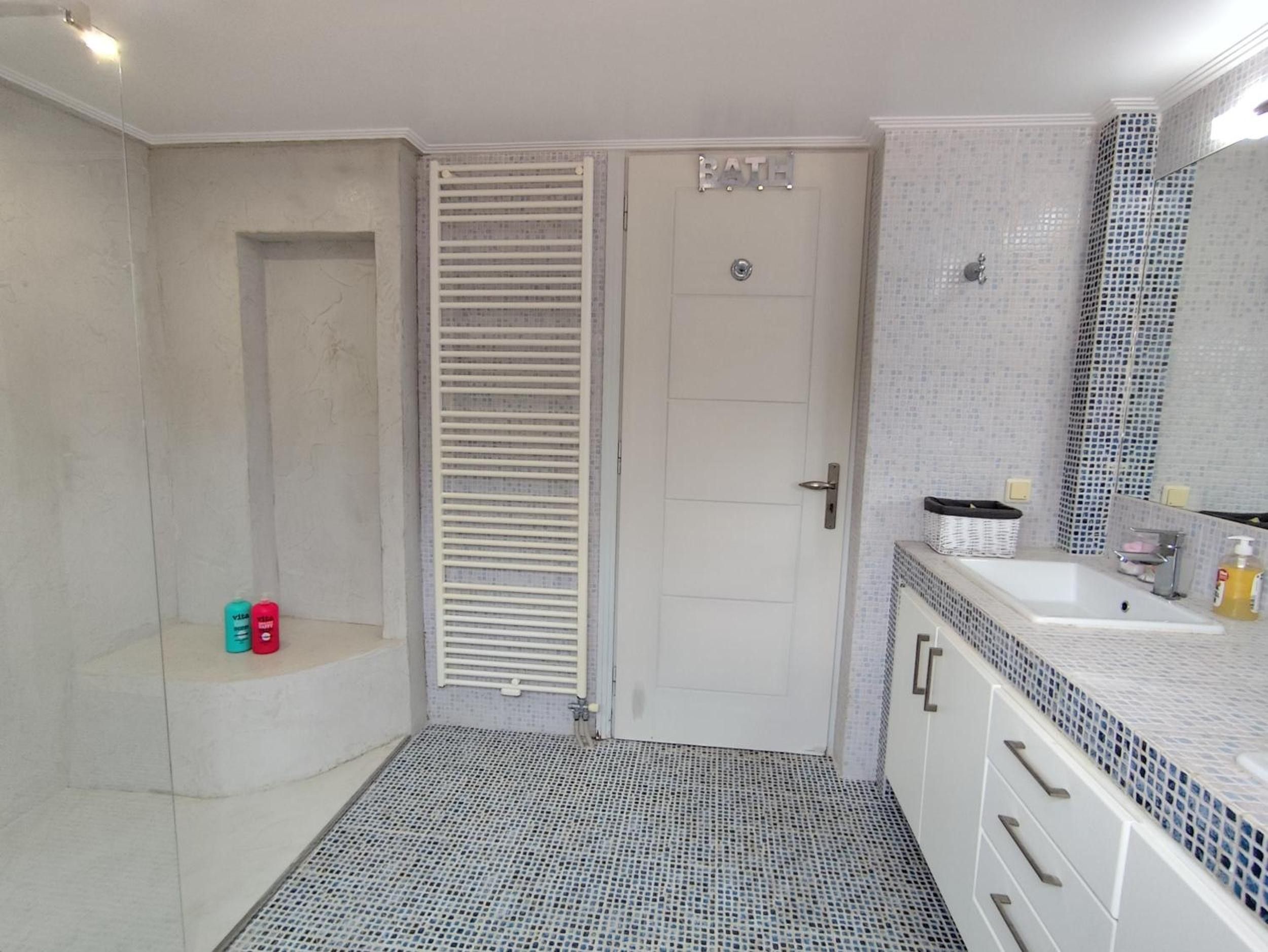 A bathroom with a white door, a shower area, a sink with a mirror, and a tiled floor.