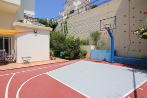 Un terrain de basket en plein air avec un mur d’escalade, une terrasse avec des chaises et un bâtiment en arrière-plan.