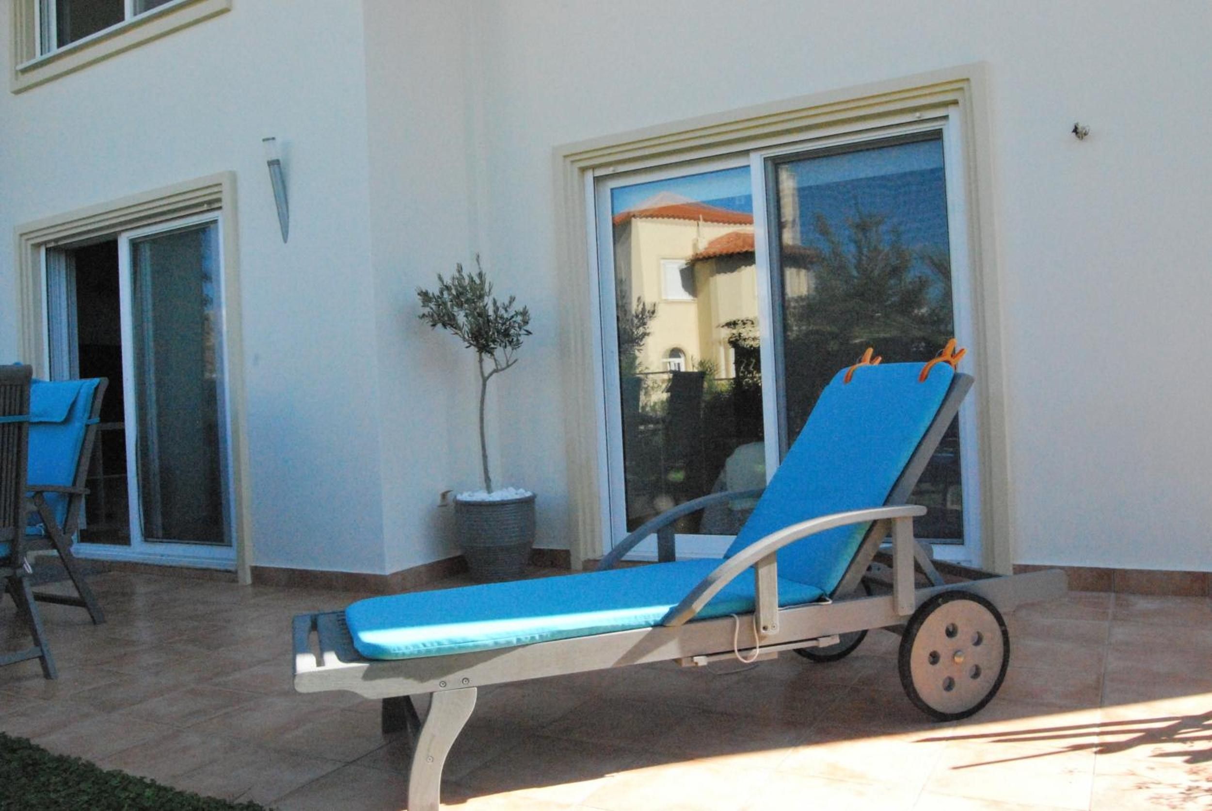 A sun lounger with wheels, a potted plant, and a sliding glass door leading to a patio area.
