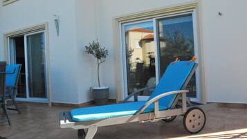A sun lounger with wheels, a potted plant, and a sliding glass door leading to a patio area.
