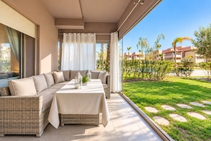Ein modernes Wohnzimmer mit einer Couch, einem Tisch und Blick auf einen gepflegten Garten sowie Gebäude.