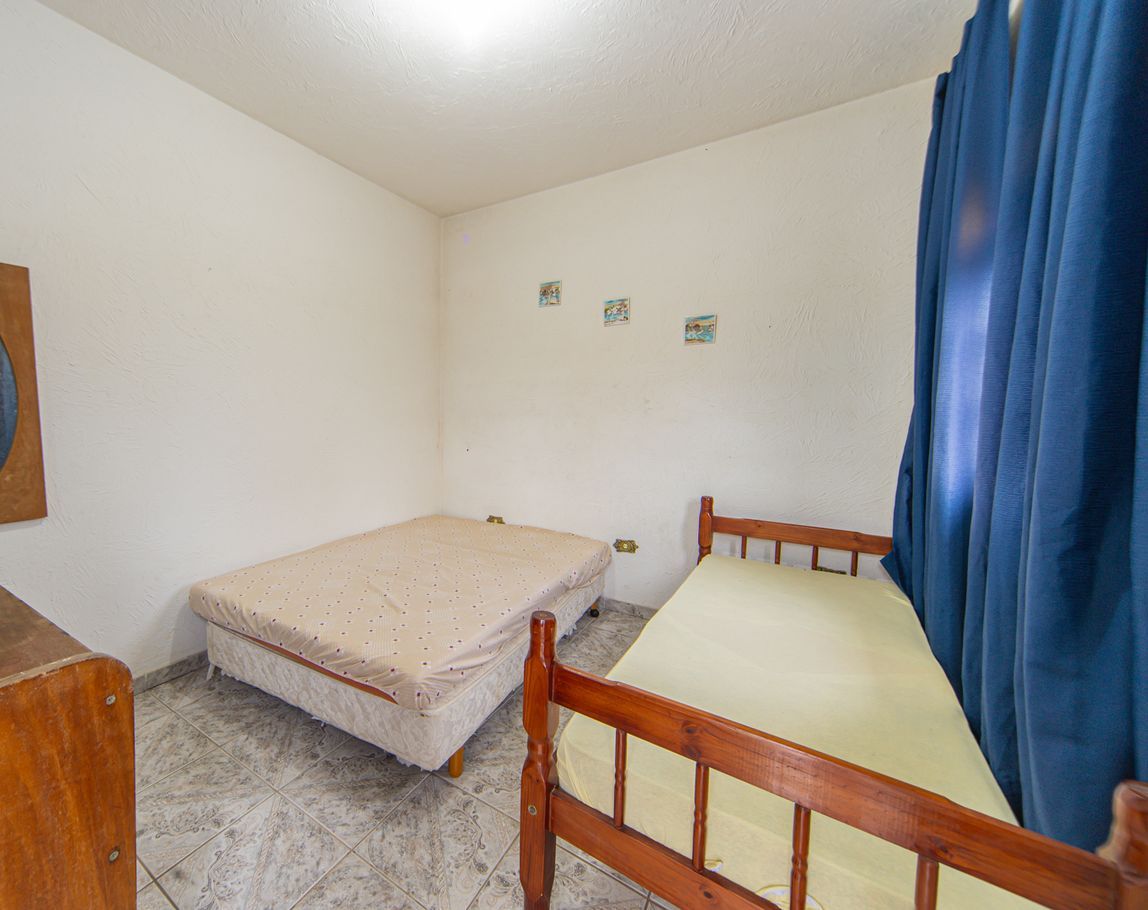 Une petite chambre avec un lit simple, une tête de lit en bois, un matelas et un rideau bleu.