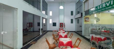 A spacious indoor area with multiple tables and chairs, a glass partition, and a sign indicating self-service options.