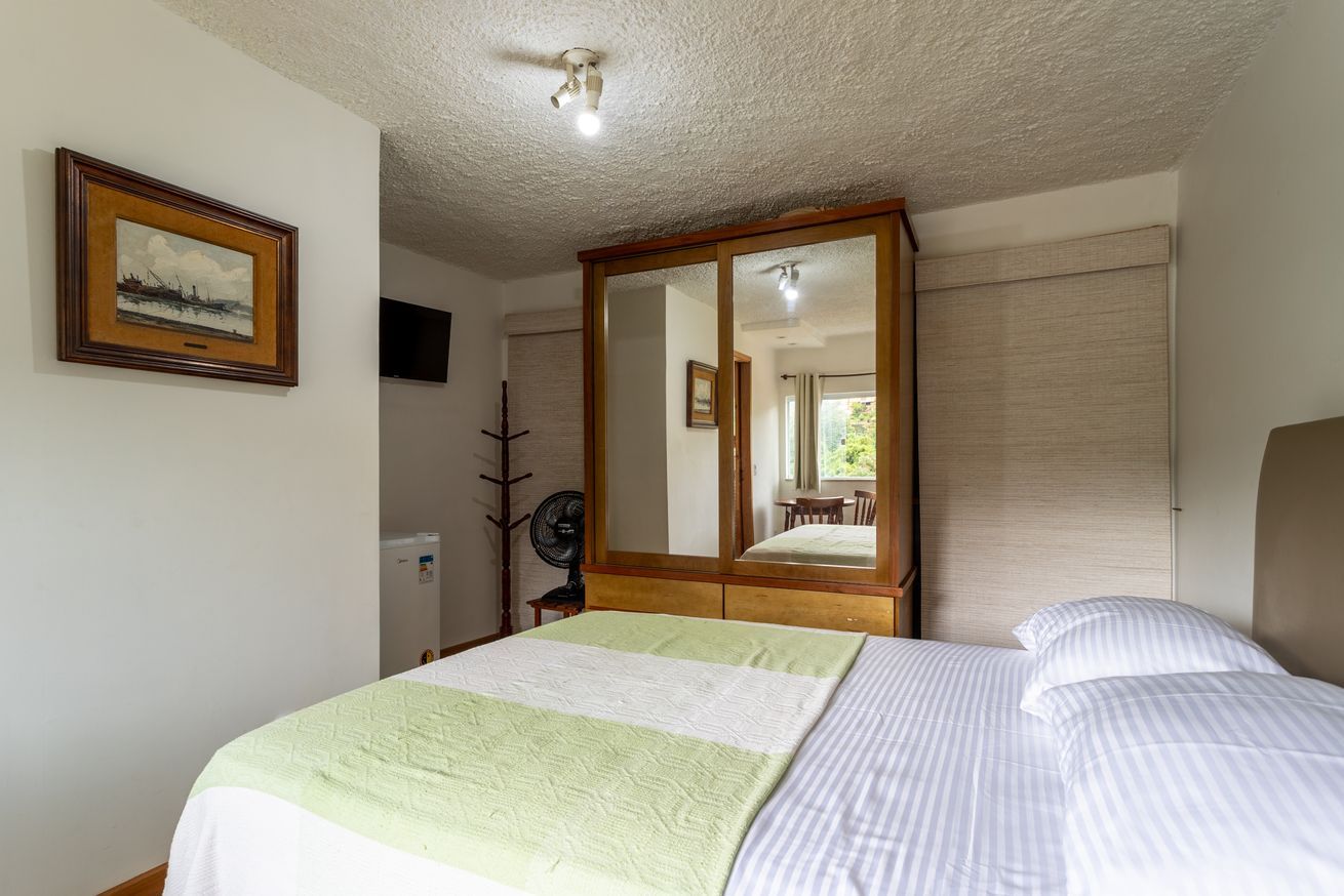 A bedroom with a bed, a wooden wardrobe, a mirror, and a framed picture on the wall.